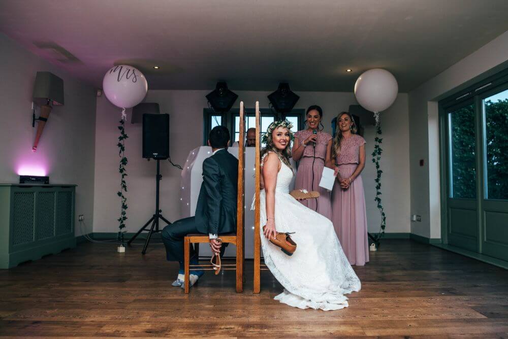 The bride and groom sit with their backs against each other as they hold their partners shoes.