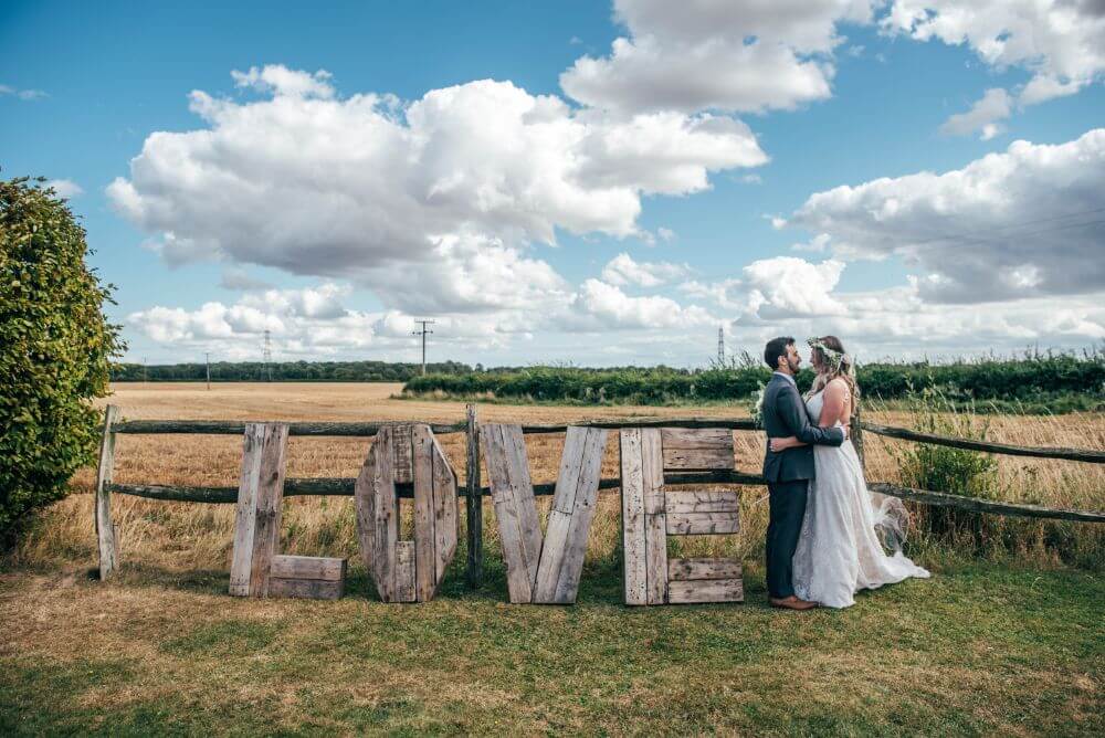 The couple embrace next to a big wooden sign that spells "LOVE".