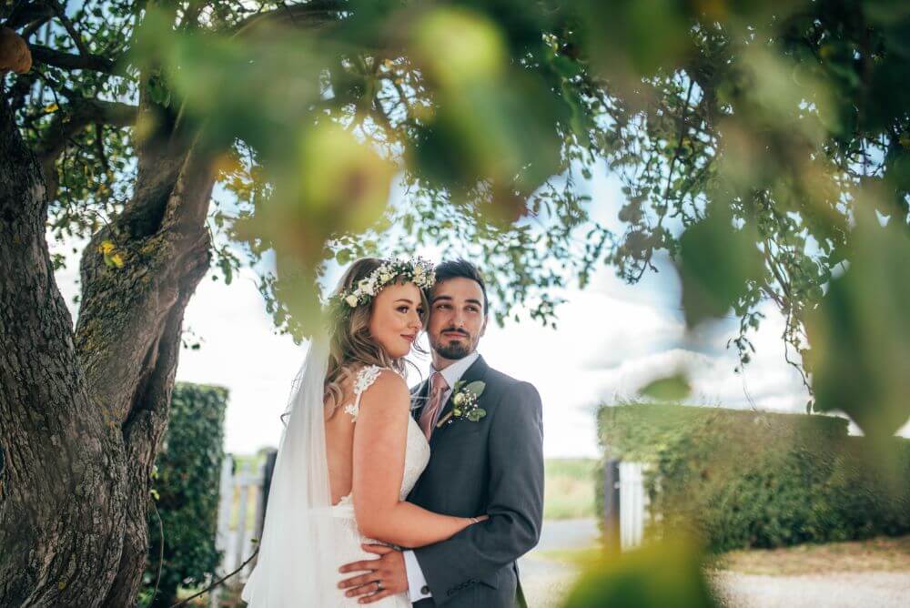 The bride and groom embrace underneath a big tree.