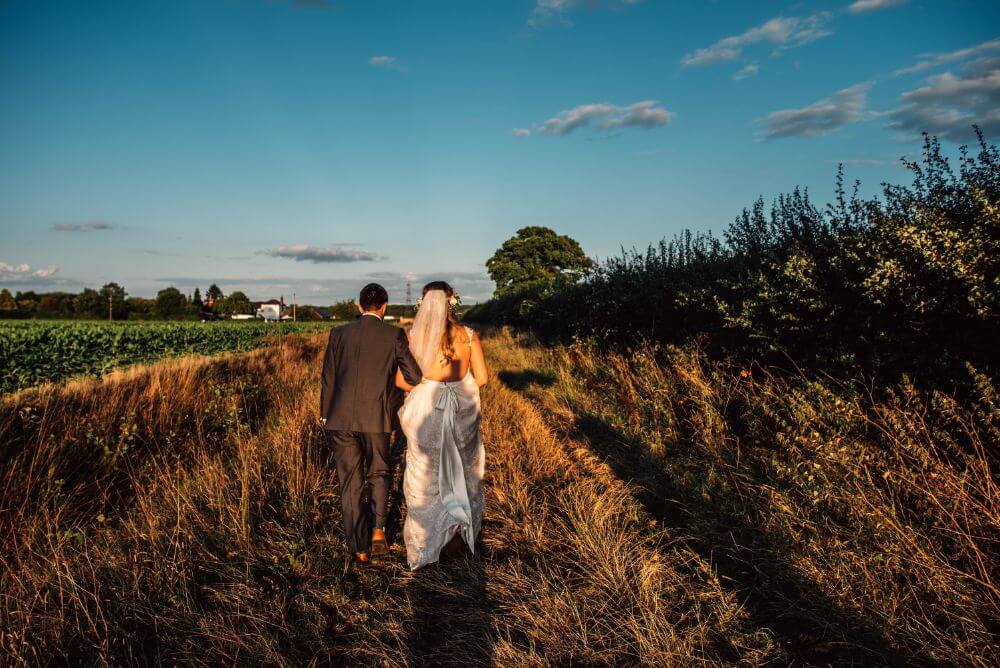 The bride and groom walk outside in the middle of a field.