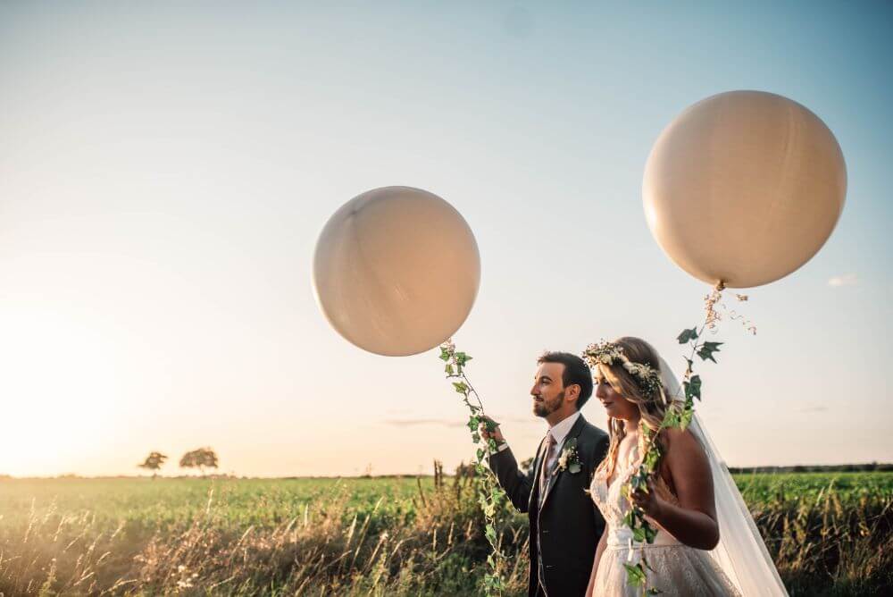 The bride and groom walk outside holding big white balloons.