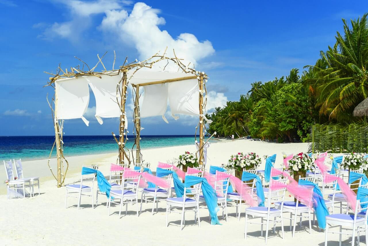 Pink and blue ribbons tied to wedding chairs at beautiful beach wedding