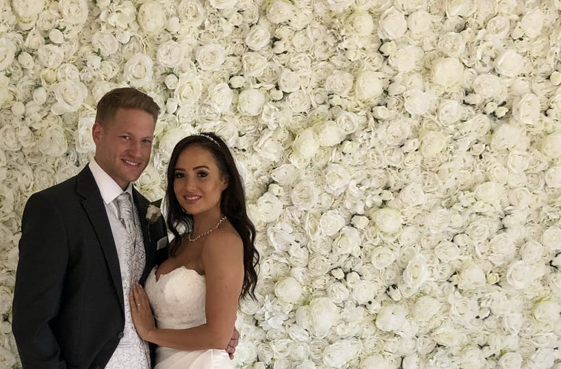 White flower wall with married couple standing in front of flower wall