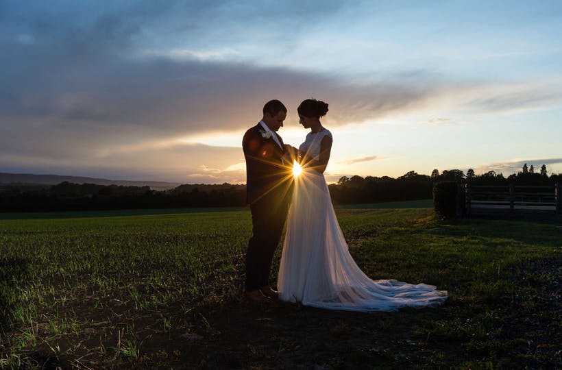 Married couple  standing in field at sunset