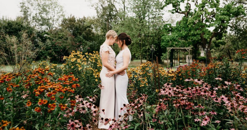 Brides surrounded by tall, colourful flowers in a garden, touching foreheads and looking at each other