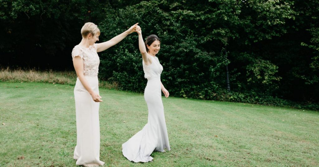 Brides holding hands in garden, mid dance