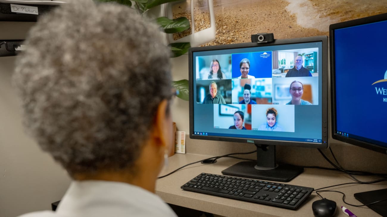 back of a doctors head in an online meeting on a computer with multiple people