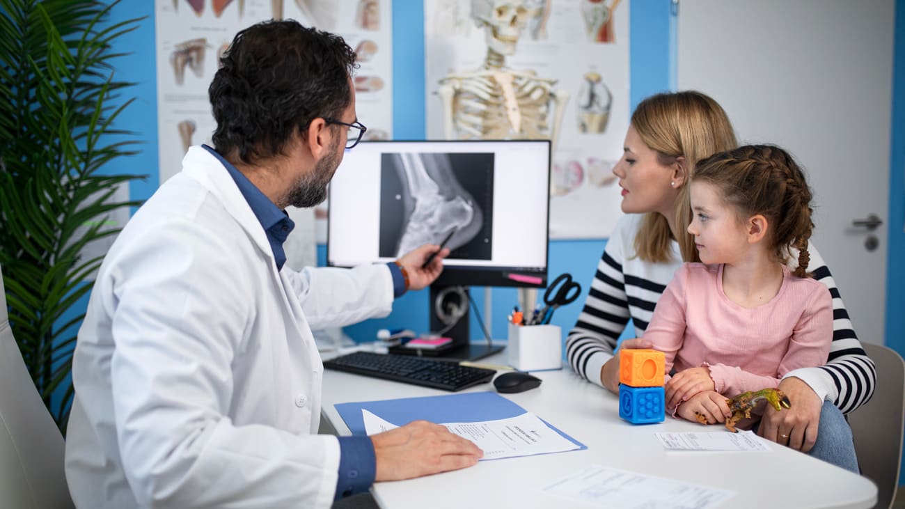 Healthcare provider reviewing an ankle X-ray with a child and caregiver in an exam room.