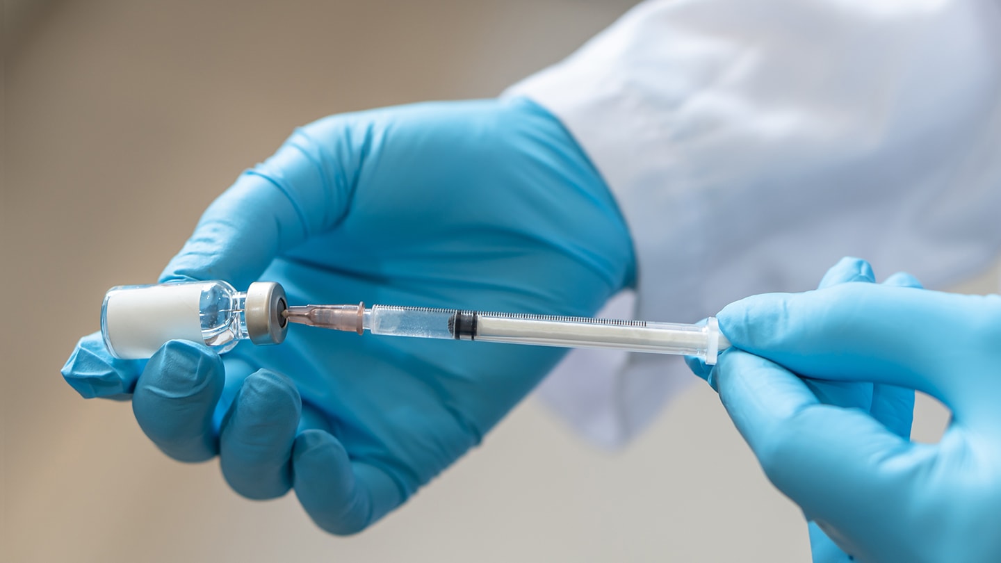 Clinician preparing medication with a syringe and vial.