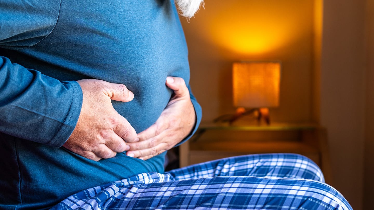 Person sitting on a bed holding their abdomen.
