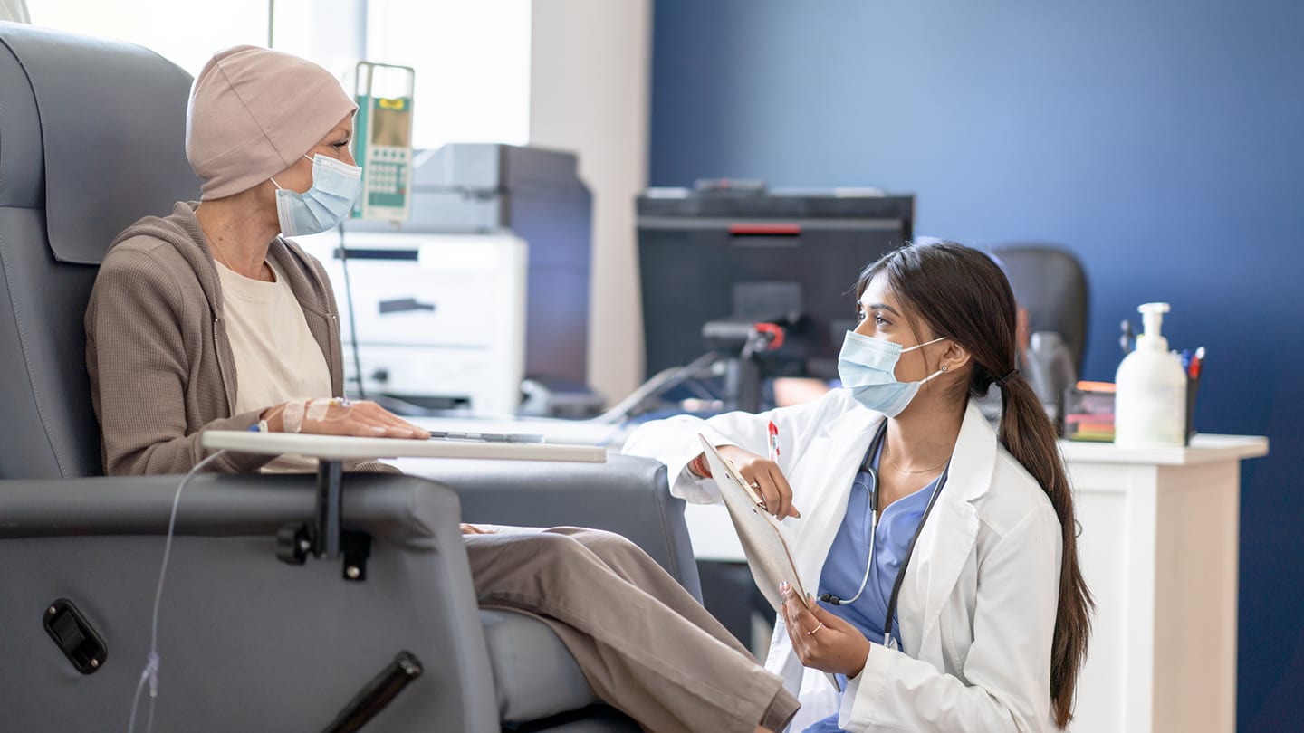 Patient receiving cancer treatment while a clinician reviews notes.