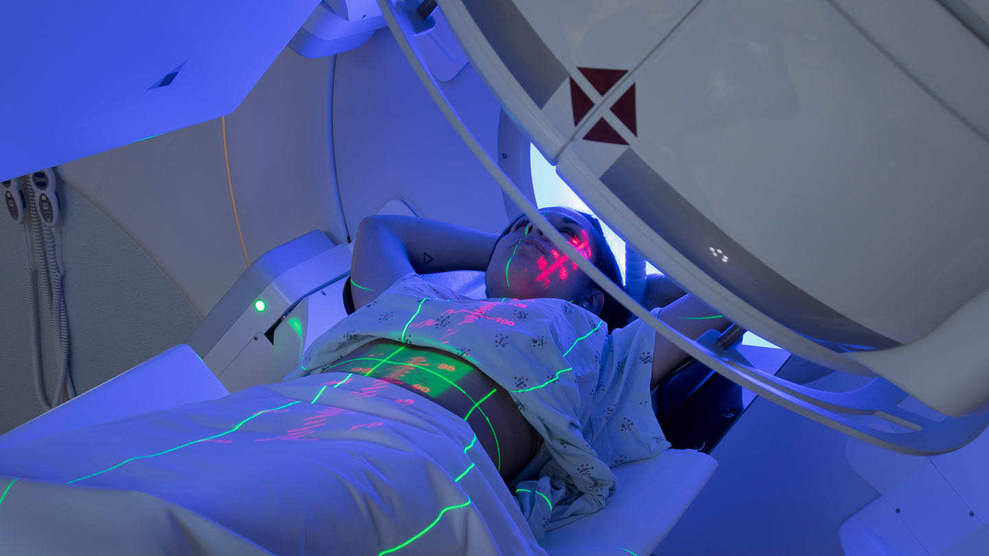Patient undergoing radiation therapy beneath a treatment machine.