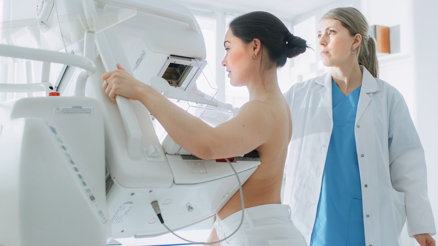 Patient undergoing breast imaging with a clinician assisting.