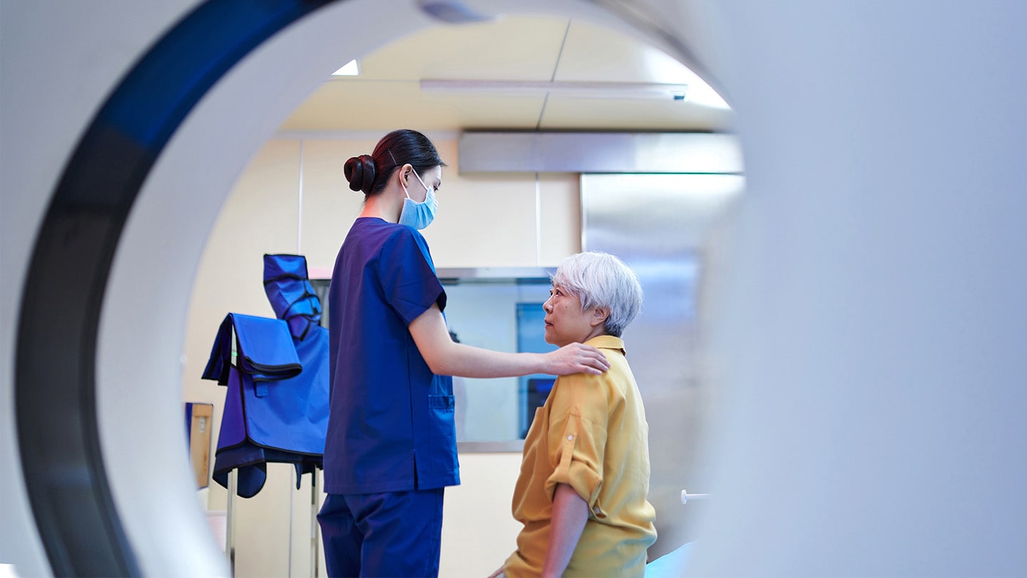 Older patient speaking with a clinician near a medical scanner.
