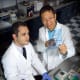 A doctor and a resident, both in white lab coats, look at a transparent blue paper that shows proteins expressed by ovarian cancer cells.