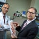 Abhay Moghekar, dressed in a white lab coat, and Mark Luciano, wearing a dark blue suit, holding a 3D model of the brain and neck.