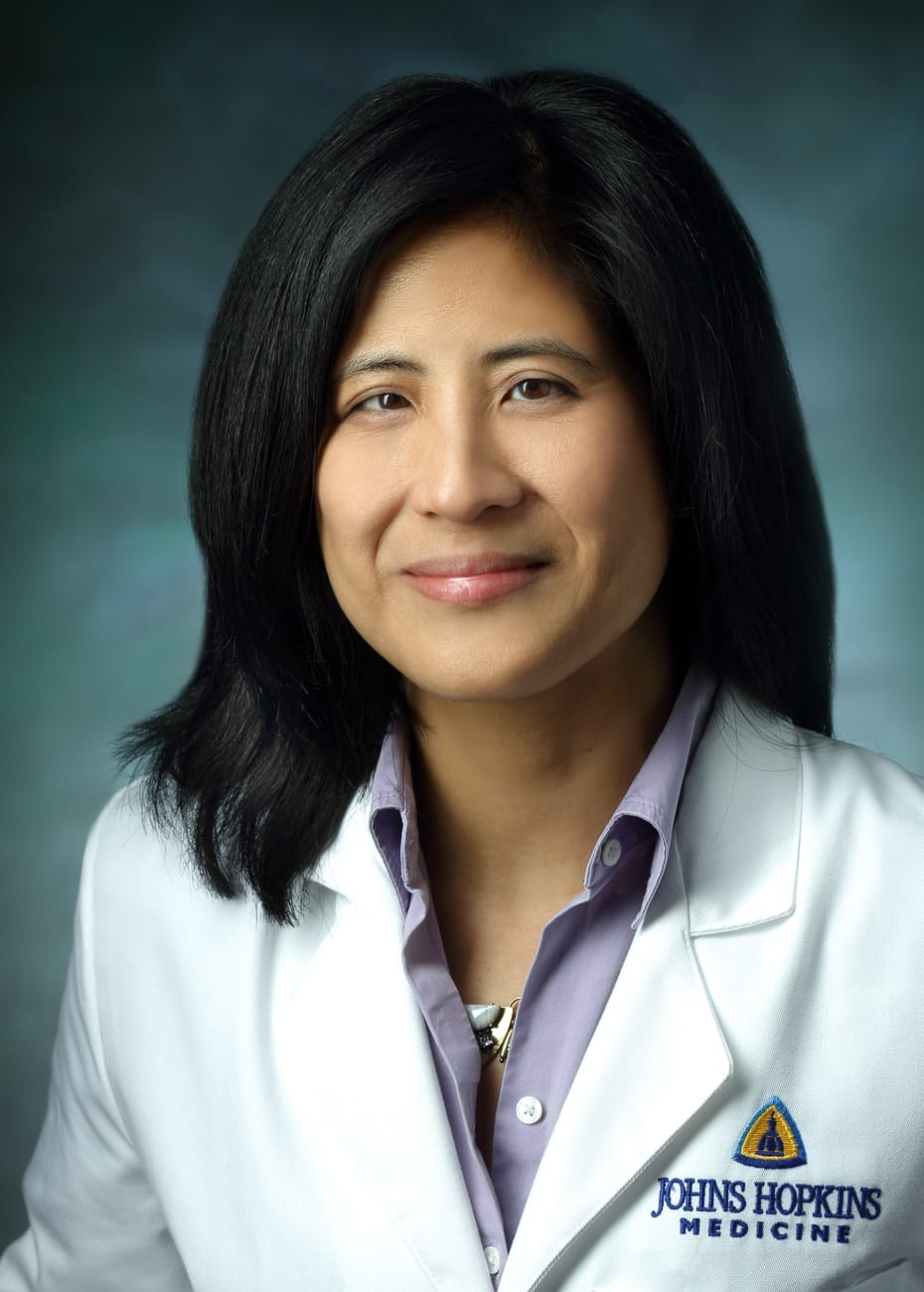 Gina Adrales, in a formal portrait, wearing a white lab coat and light purple button down shirt