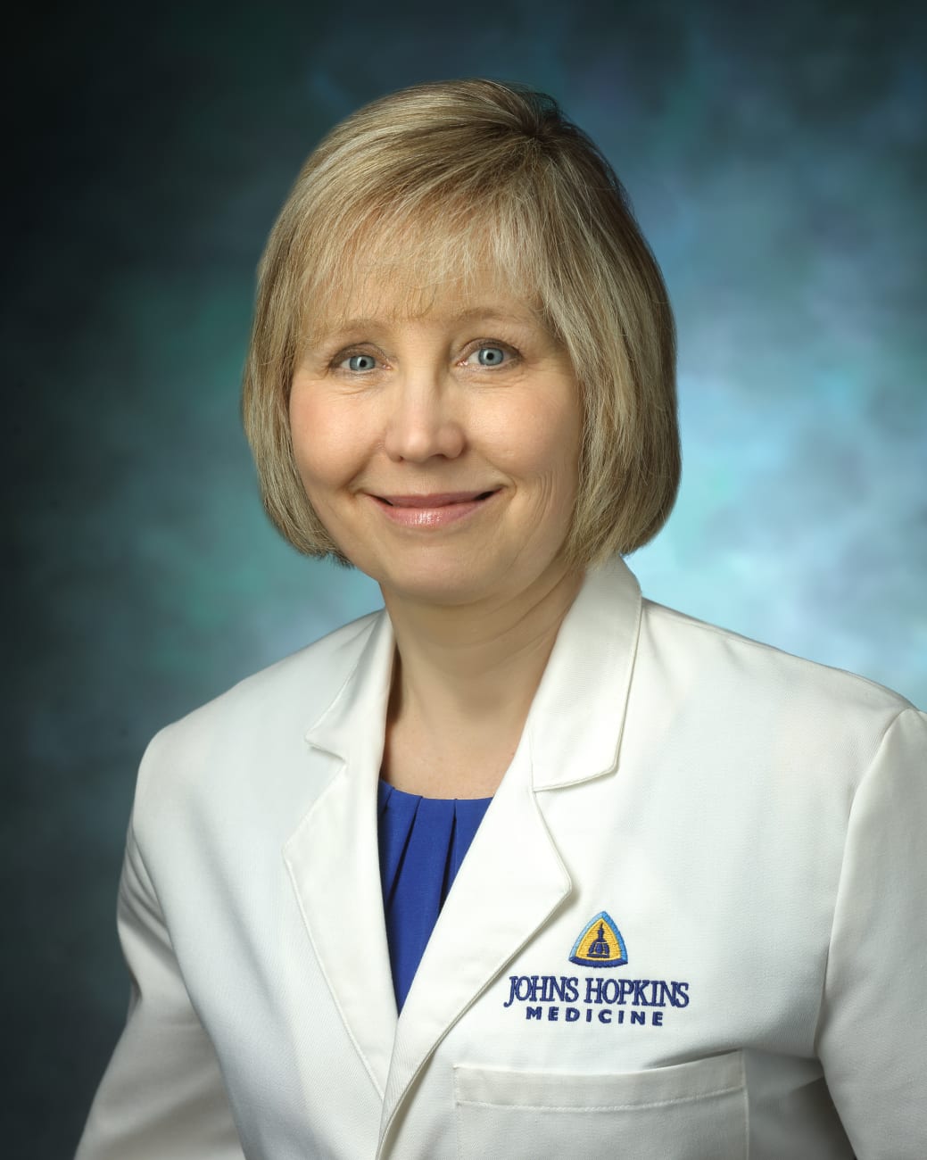 Valerie Baker, in a formal portrait, wearing a white lab coat and blue blouse