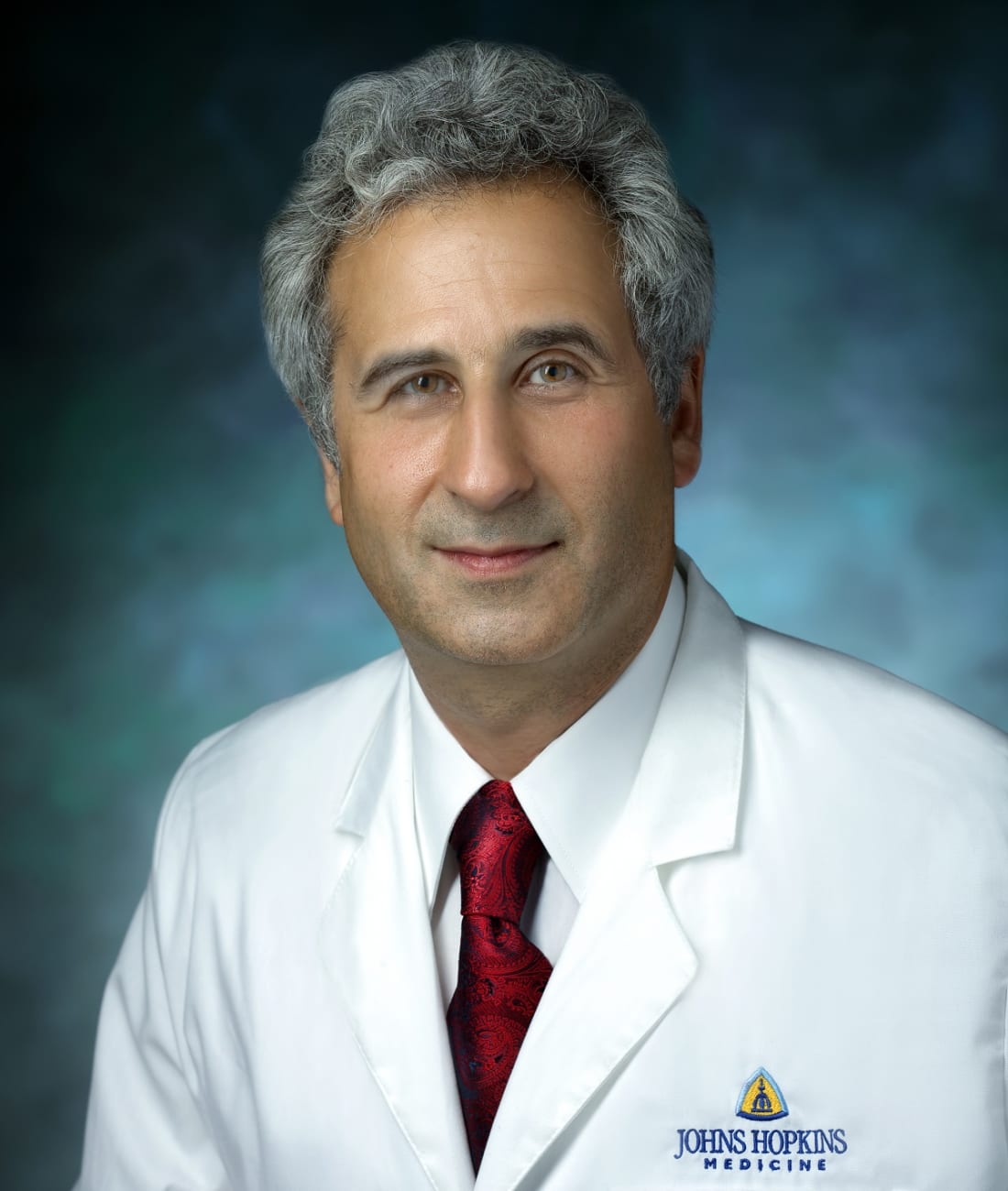 Ahmet Baschat, in a formal portrait, wearing a white lab coat, white button down shirt and red tie.