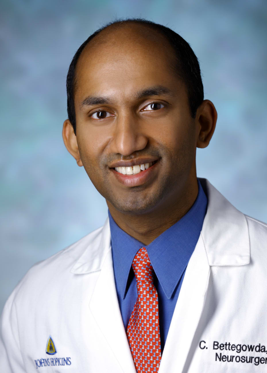 Chetan Bettegowda, in a formal portrait, wearing a white lab coat, red tie and blue button-down shirt.