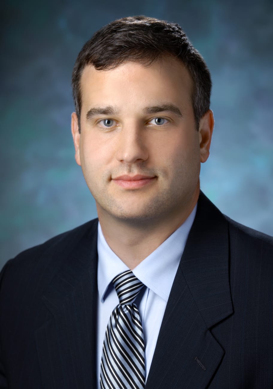 Eric Jackson, in a formal portrait, wearing a dark blue suit, light blue button down shirt and blue, black and white striped tie