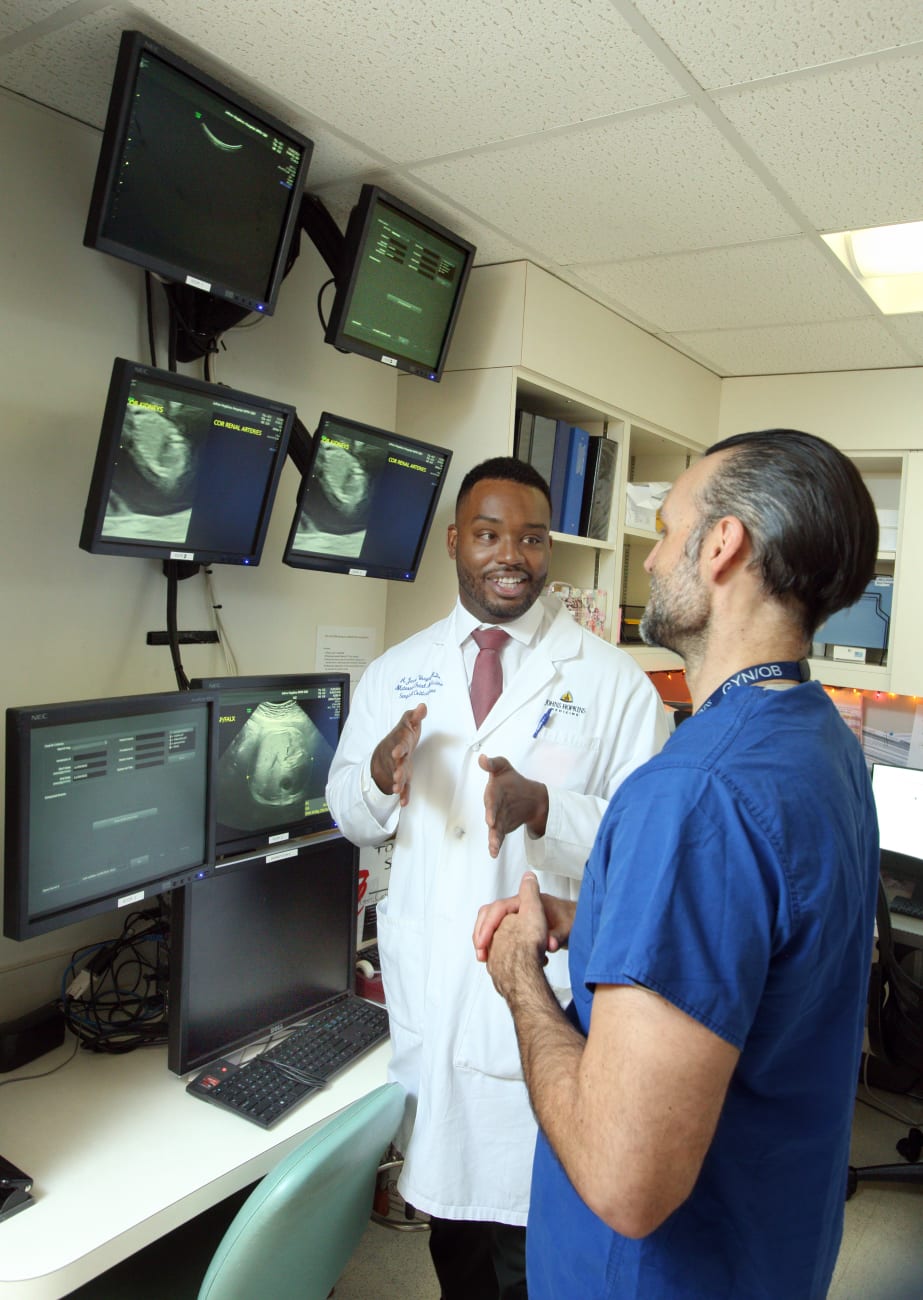 Jason Vaught and Torre Halscott speak to each other in a room with multiple computer monitors showing an ultrasound