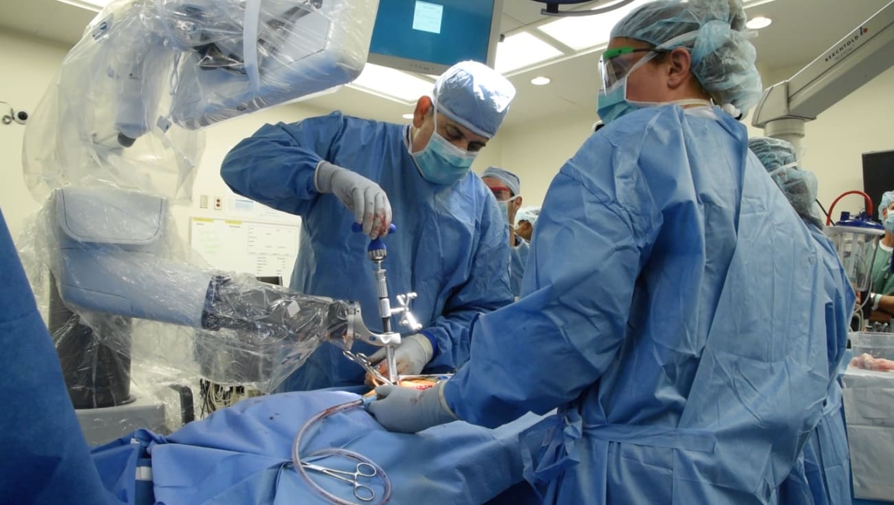 Nicholas Theodore, in an operating room wearing a surgical gown, camp and gloves, performs a robotic spine surgery