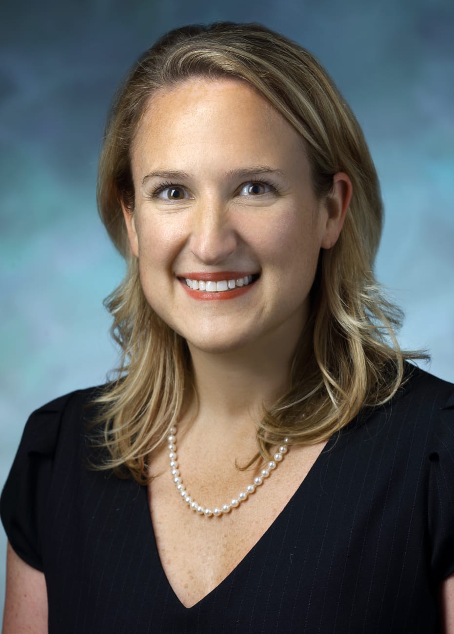 Rebecca Stone, in a formal portrait, wearing a black shirt and pearl necklace