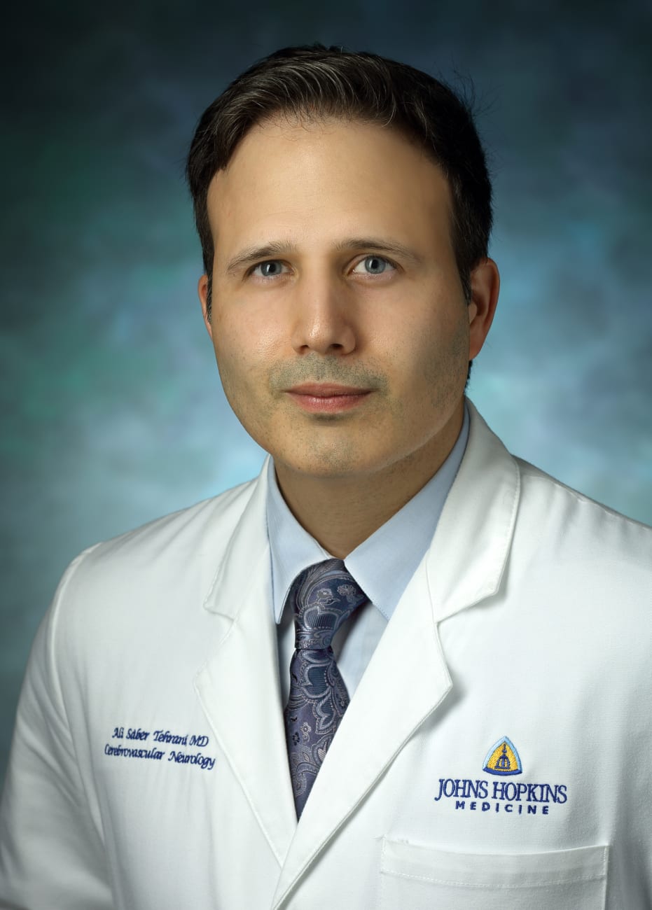 Ali Tehrani, in a formal portrait, wearing a white lab coat,  light blue button down shirt and blue paisley tie 