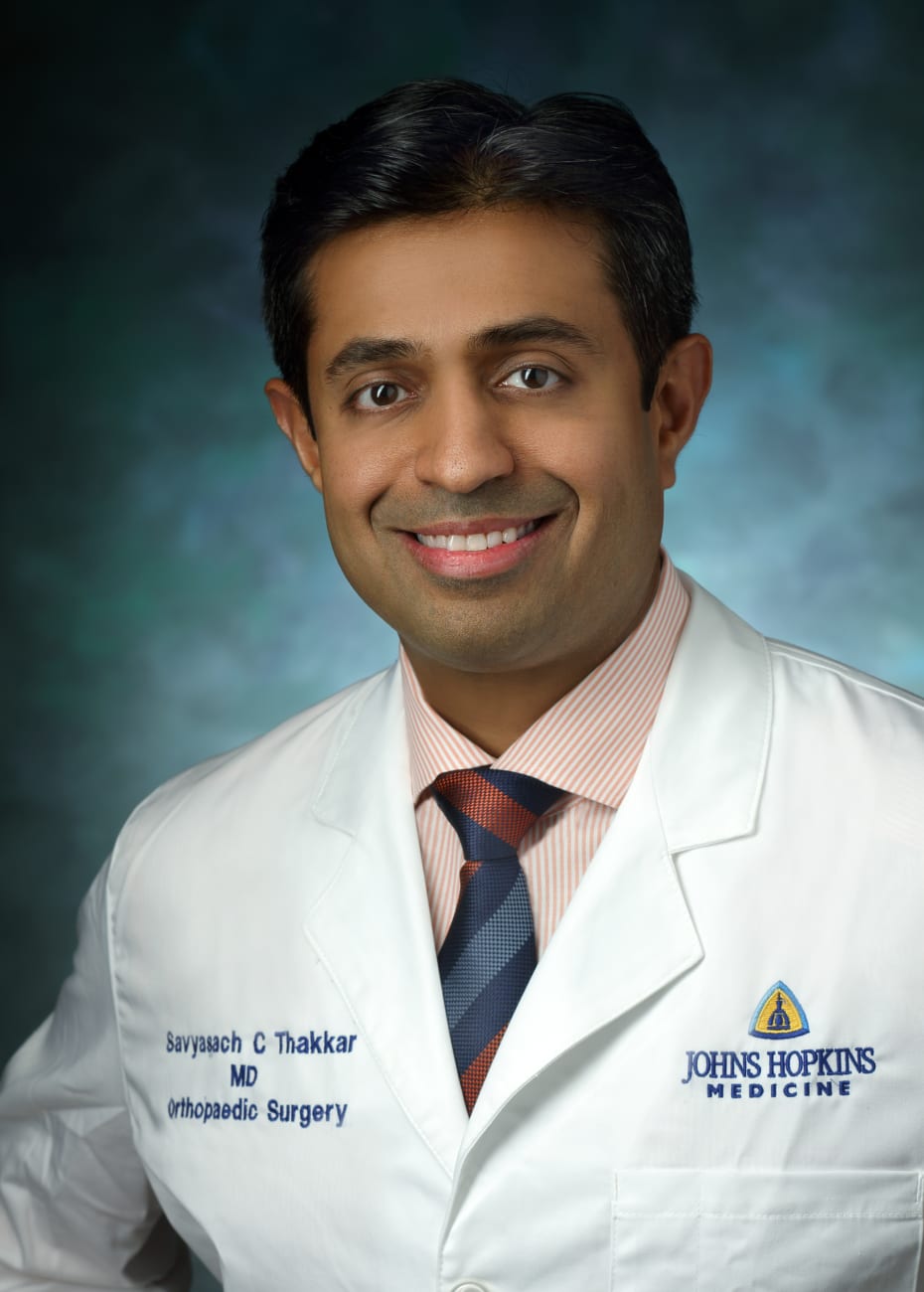 Savyasachi Thakkar in a formal portrait, wearing a white lab coat, orange and white striped button down shirt and orange and blue tie