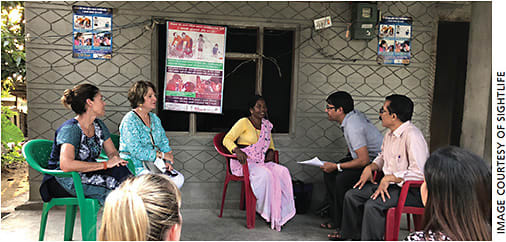 A community health worker sits with the corneal prevention program staff and SightLife Advocates to review the log books where she tracks patient information. The poster attached to her home signifies that community members can seek medical attention there.