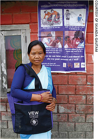 A community health worker in Nepal showcases a prevention awareness poster at her home.