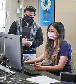 At the front desk, Ronald Chevez, ophthalmic technician assistant, is being trained by Stephanie Tran, patient relations specialist.