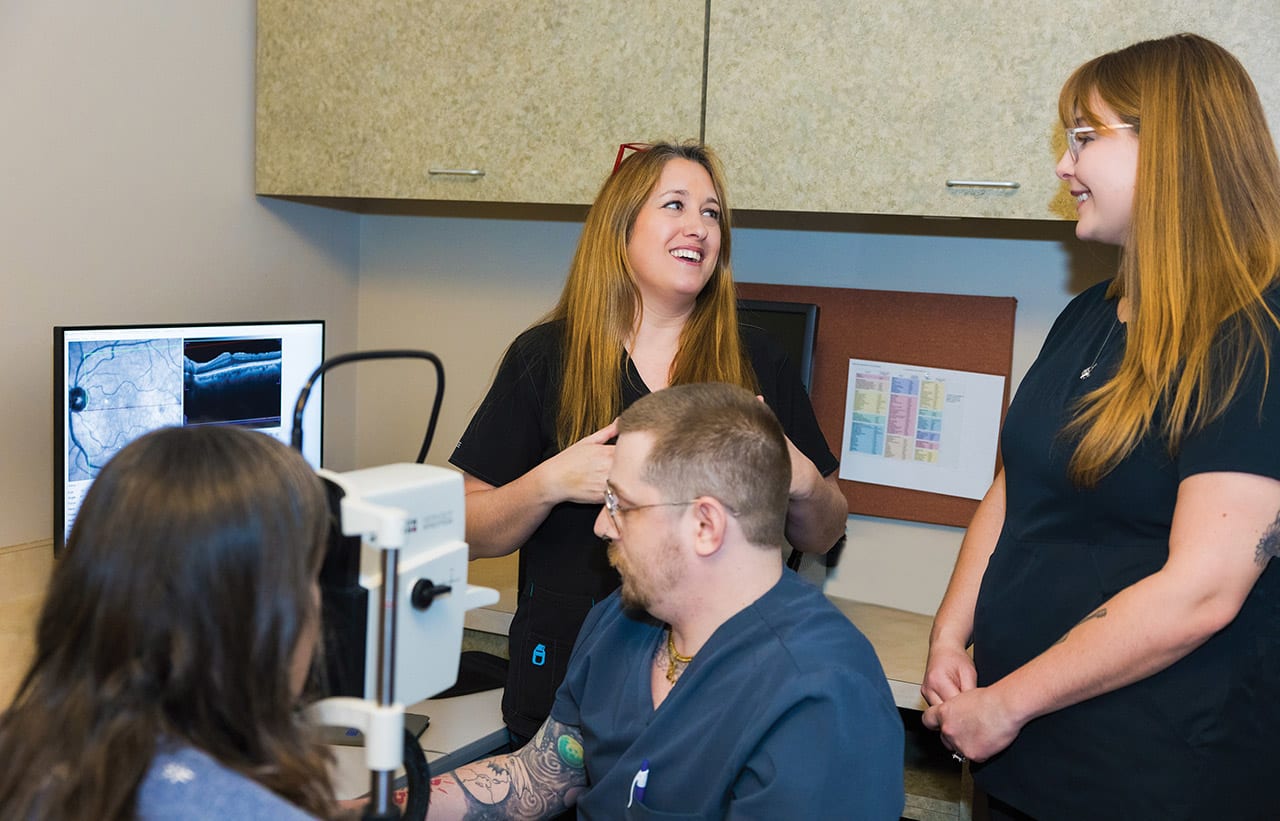 Margaret Whelehan (standing, left) helps train new photographer Karissa Kuhl (right) while Owen Maloy (seated) performs an OCT scan on a patient.