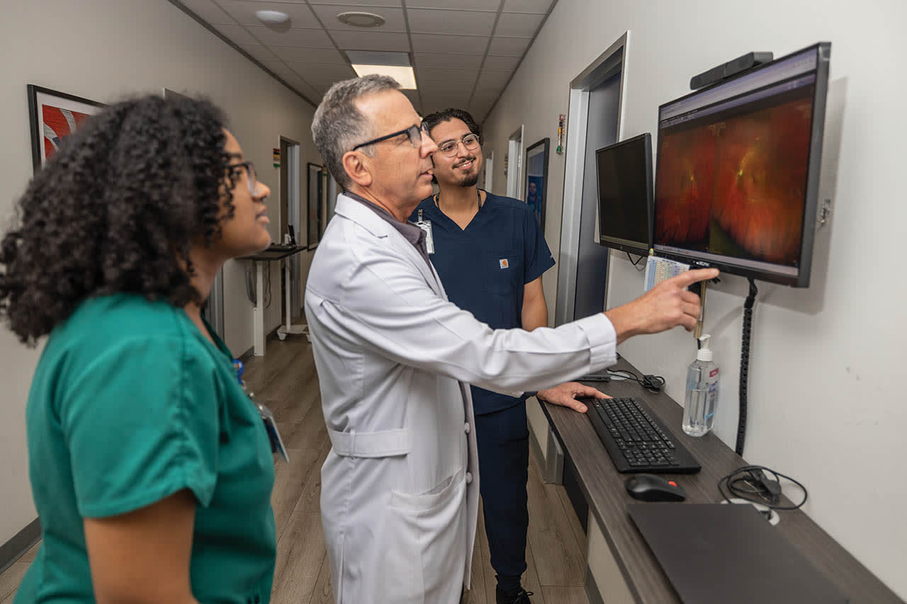 Dr. Jose A. Martinez teaching his clinic team, Braelyn Mouton and Brian Perez, about retinal pathology via image review.