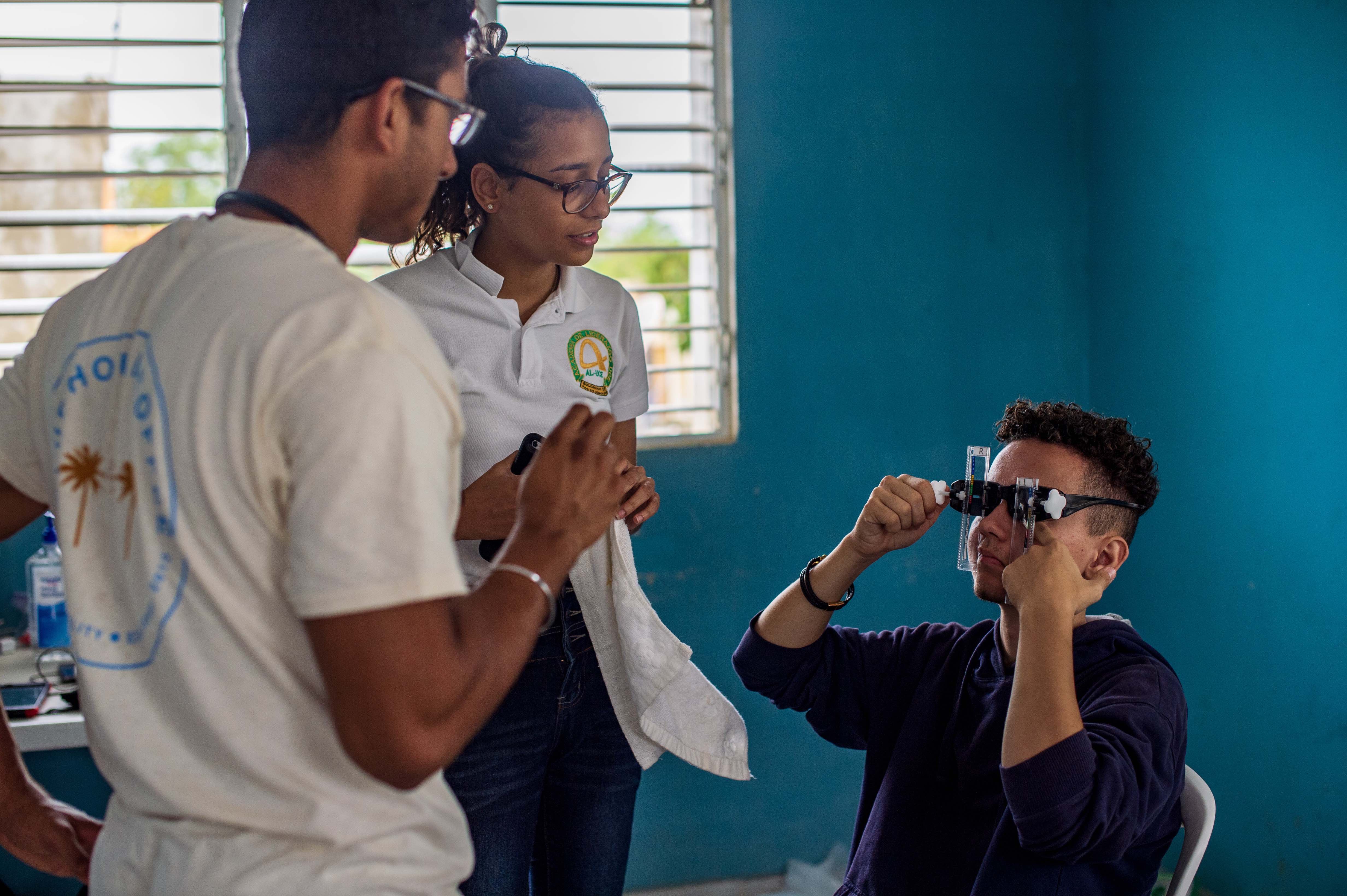 University of Arizona College of Medicine-Phoenix first-year medical student Neeraj Vij (left) teaches AL-UCE (Academia de Liderazgo-Universidad Central del Este, San Pedro De Macoris, Dominican Republic) students Lisbeth Vidal (center) and Damian Kacper (right) to use the USee self-refracting glasses. AL-UCE students serve as additional translators for the University of Arizona College of Medicine groups.
