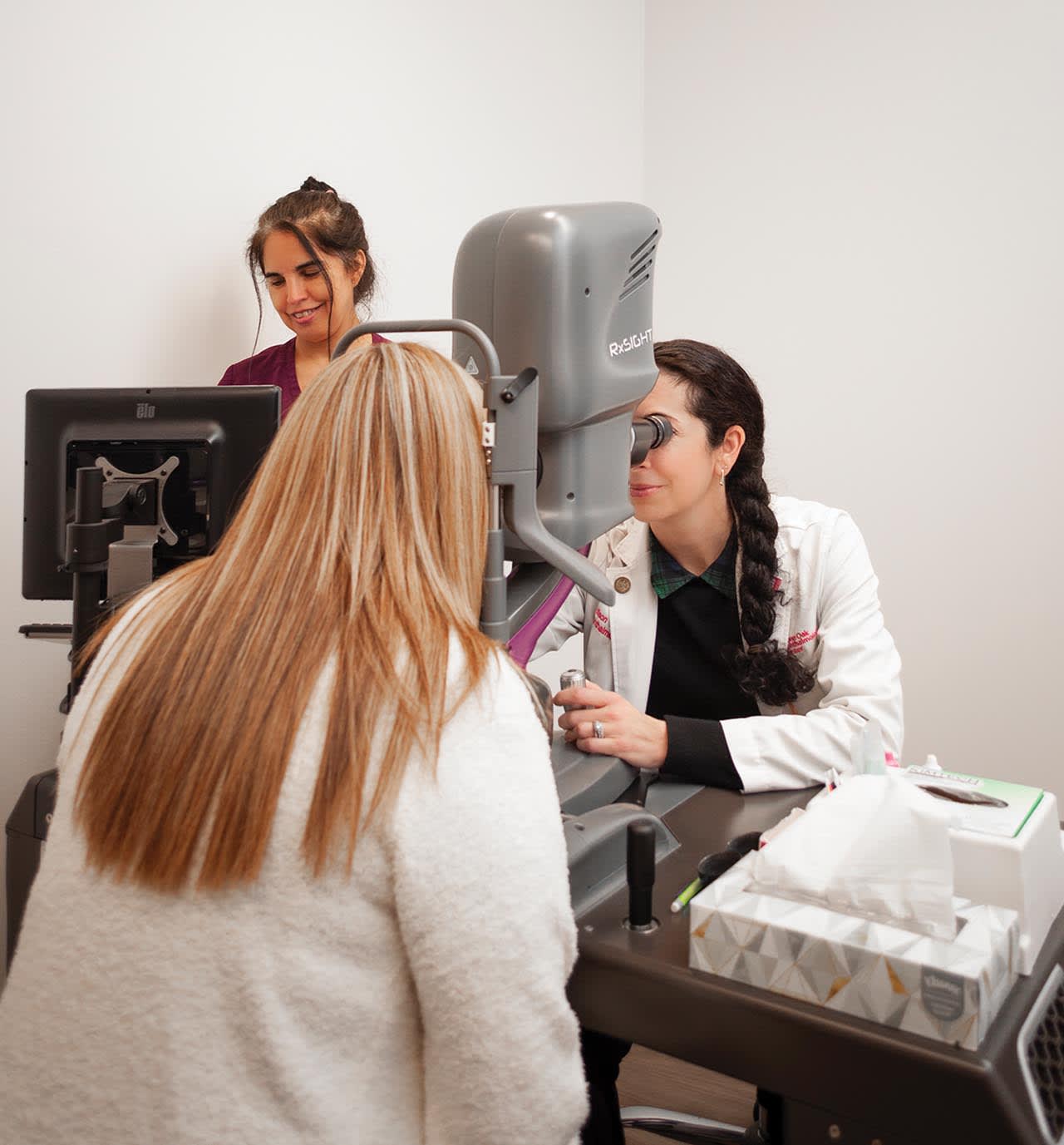 Dr. Allison Young sitting at the Light Delivery Device examining a patient, with scribe and assistant, Debra Benavides, to her right.