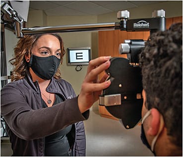 At the phoropter, Megan McCray, OSC, ophthalmic assistant, checks a patient’s visual acuity after a manifest refraction has been performed.