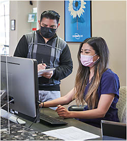 At the front desk, Ronald Chevez, ophthalmic technician assistant, is being trained by Stephanie Tran, patient relations specialist.