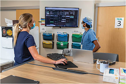 Murtaza Adam, MD, vitreoretinal surgeon, and Savannah Johnson, ophthalmic technician (left), review clinical workflow. By using an electronic dashboard, they can determine whether the clinic is running on time and which patient to see next.