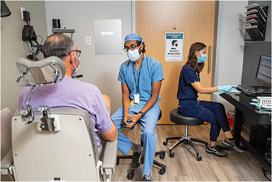 Murtaza Adam, MD, vitreoretinal surgeon, discusses a diagnosis and treatment plan with a patient while Kayla Cisneros, ophthalmic technician (right), documents the encounter.