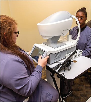 Caitlin Jeansonne, technician (left), familiarizes herself with the wavefront visual assessment system (Visionix VX130, Luneau Technology USA), as Allison Watts, technician (right), observes.