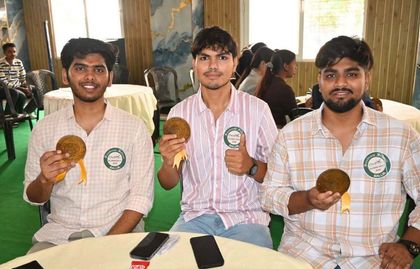 Three alumni seated at a table, holding their commemorative medallions and wearing the meet’s Pradiptam badges.