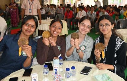Four alumnae at a table holding their medallions, a Pradiptam 2.0 table card in front of them.