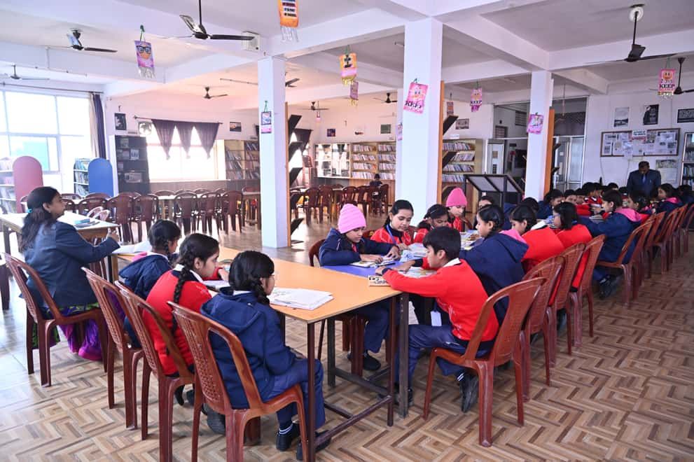 Students of Sunbeam School Ballia reading at the long tables of the library, a member of staff at the head of the row