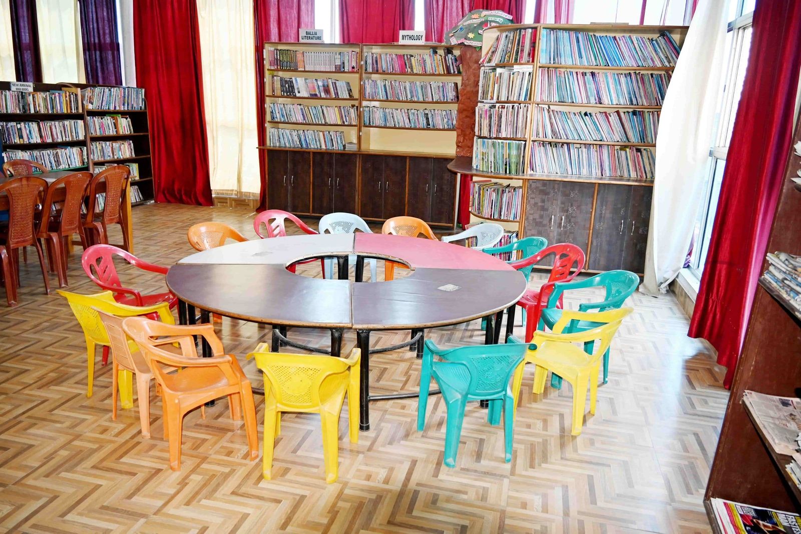 The library at Sunbeam School Ballia, its reading table ringed with chairs and the shelves labelled by subject.