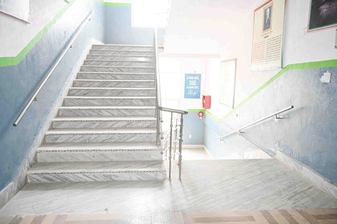 A stairwell at Sunbeam School Ballia — a marble flight rising to the landing, steel handrails either side and framed notices on the wall above