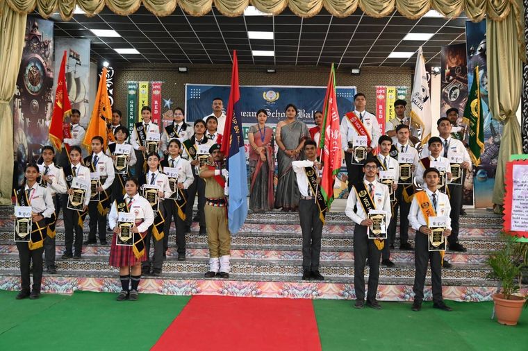 Students of Sunbeam School Ballia on stage holding framed certificates and the house flags, their sashes reading Head and Vice, with staff standing behind them.