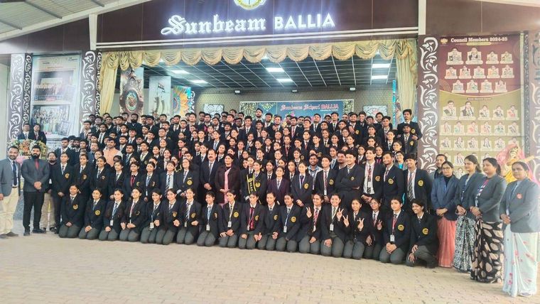 The youngest classes of Sunbeam School Ballia on stage in graduation caps and striped sashes, each holding a rolled certificate, with their teachers standing behind them.