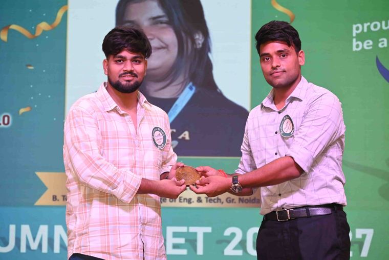 One alumnus handing a commemorative medallion to another at Pradiptam 2.0, both wearing the meet’s badges.